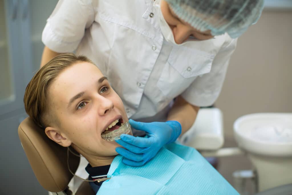 Female dentist puts on a guy patient a mouth guard (a removable orthodontic teeth alignment and correction trainer appliance) in dental office.