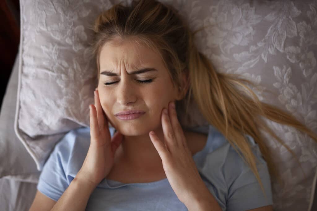 A woman lying in her bed rubbing her jaq suffering from bruxism.